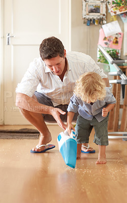 Buy stock photo A loving father crouching behind his toddler son and helping him to use a vacuum cleaner