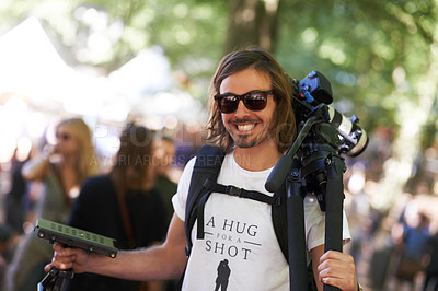 Buy stock photo A smiling photographer carrying camera and tripod at a music festival