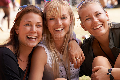 Buy stock photo Portrait of three smiling friends sitting arm in arm and at a festival