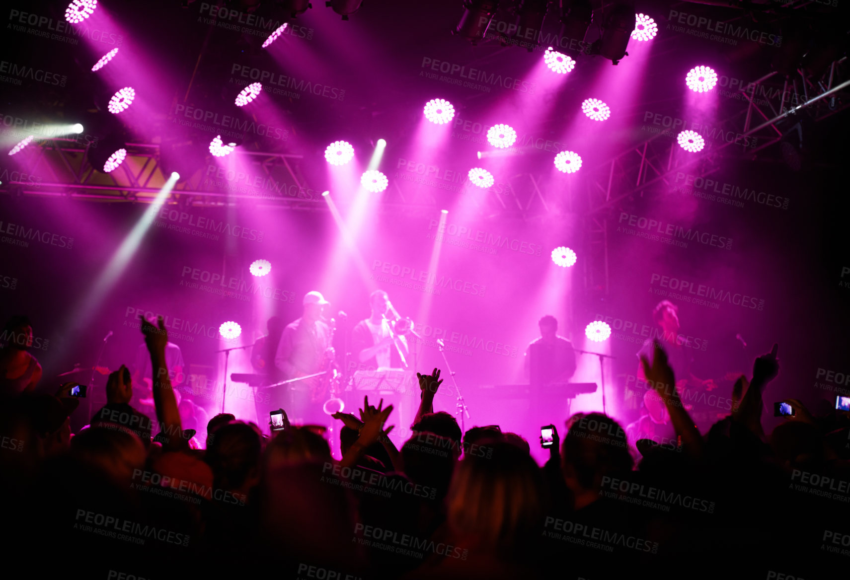 Buy stock photo Rearview of an audience with hands raised at a music festival and lights streaming down from above the stage