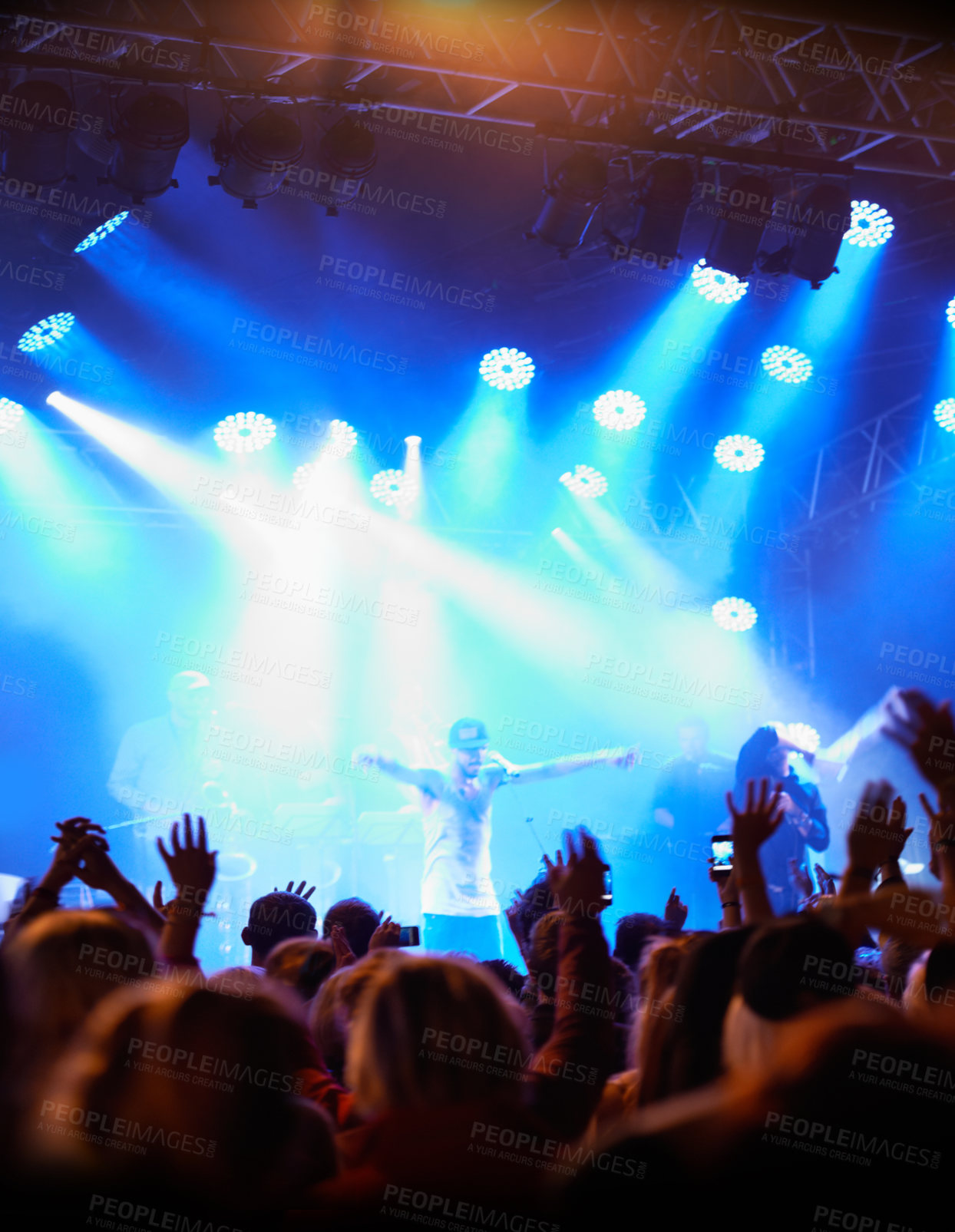 Buy stock photo Rearview of an audience with hands raised at a music festival and lights streaming down from above the stage