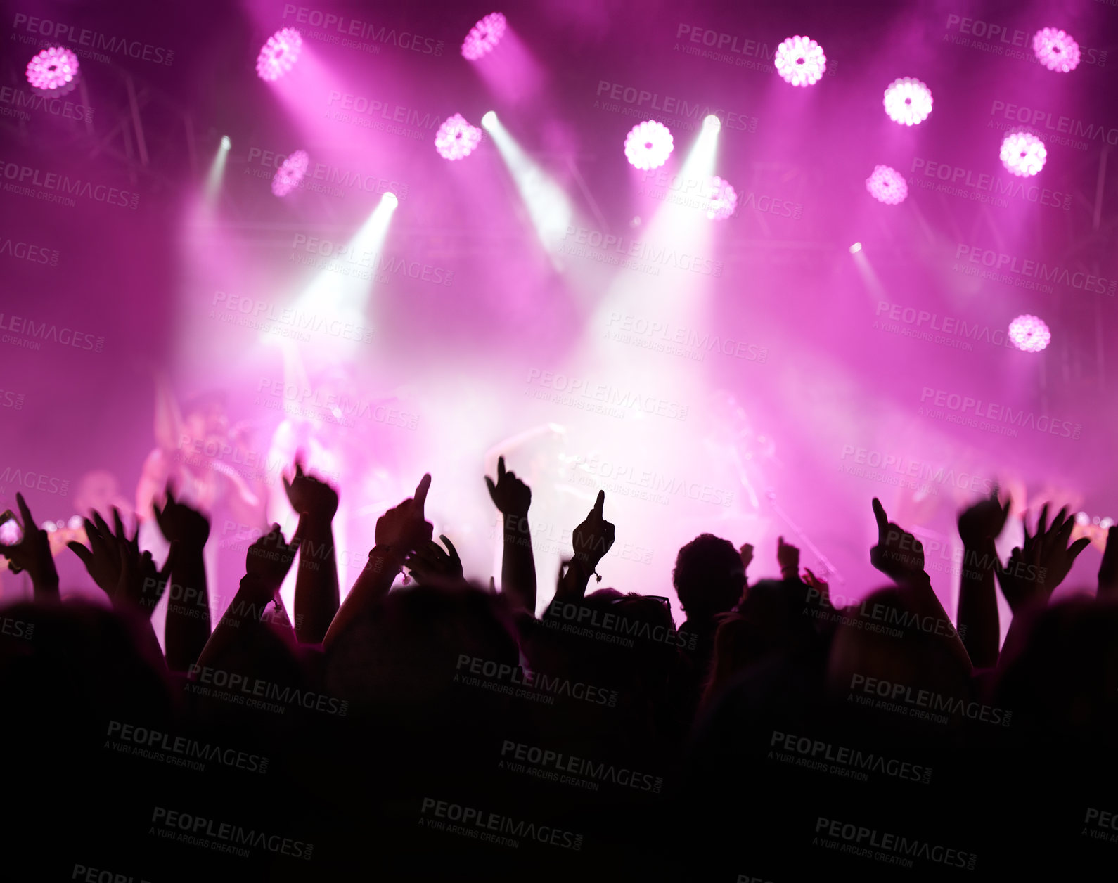 Buy stock photo Rearview of an audience with hands raised at a music festival and lights streaming down from above the stage