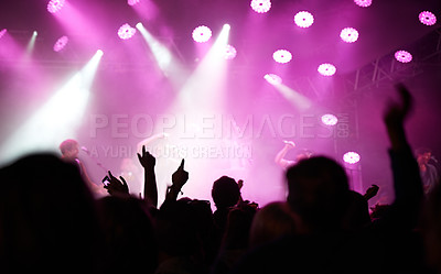 Buy stock photo Rearview of an audience with hands raised at a music festival and lights streaming down from above the stage