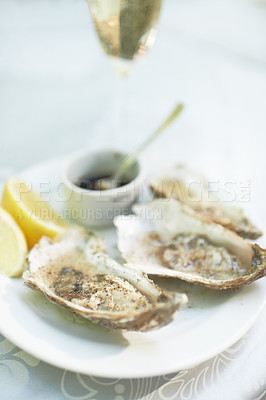 Buy stock photo Shot of a plate of oysters sitting on a table with a glass of wine