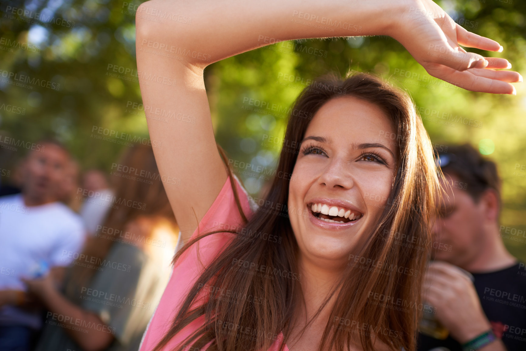 Buy stock photo A beautiful young woman smiling and enjoying music at a festival with arm raised in the air and crowd in the background