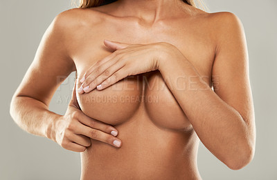 Buy stock photo Closeup studio shot of a topless woman examining her breasts against a gray background 