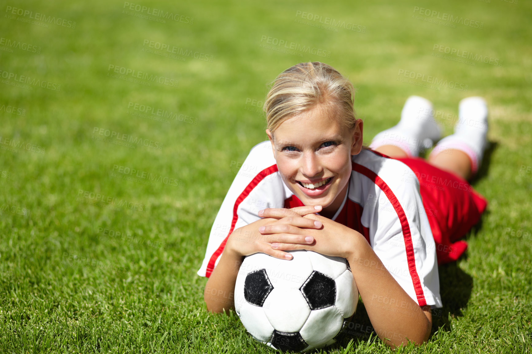 Buy stock photo Portrait of an attractive female football player lying chest down on the grass and leaning on a soccer ball