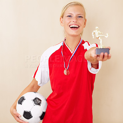 Buy stock photo Portrait of a young woman dressed in a soccer uniform holding up a trophy and a soccer ball
