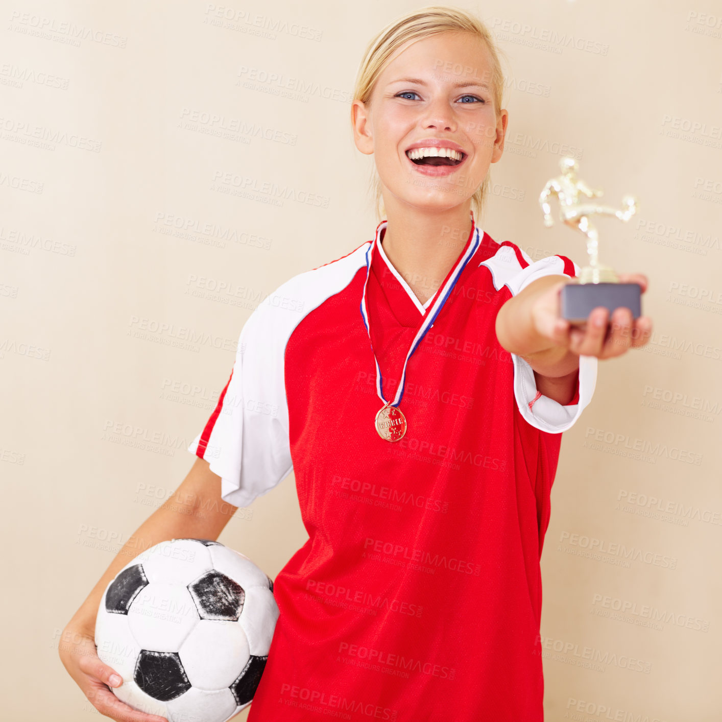 Buy stock photo Portrait of a young woman dressed in a soccer uniform holding up a trophy and a soccer ball