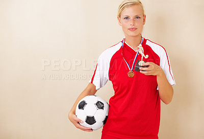 Buy stock photo Woman, soccer player and trophy portrait of a winner on a plain background for football achievement.  A young female sports person or athlete with a ball and champion medal award for winning a game