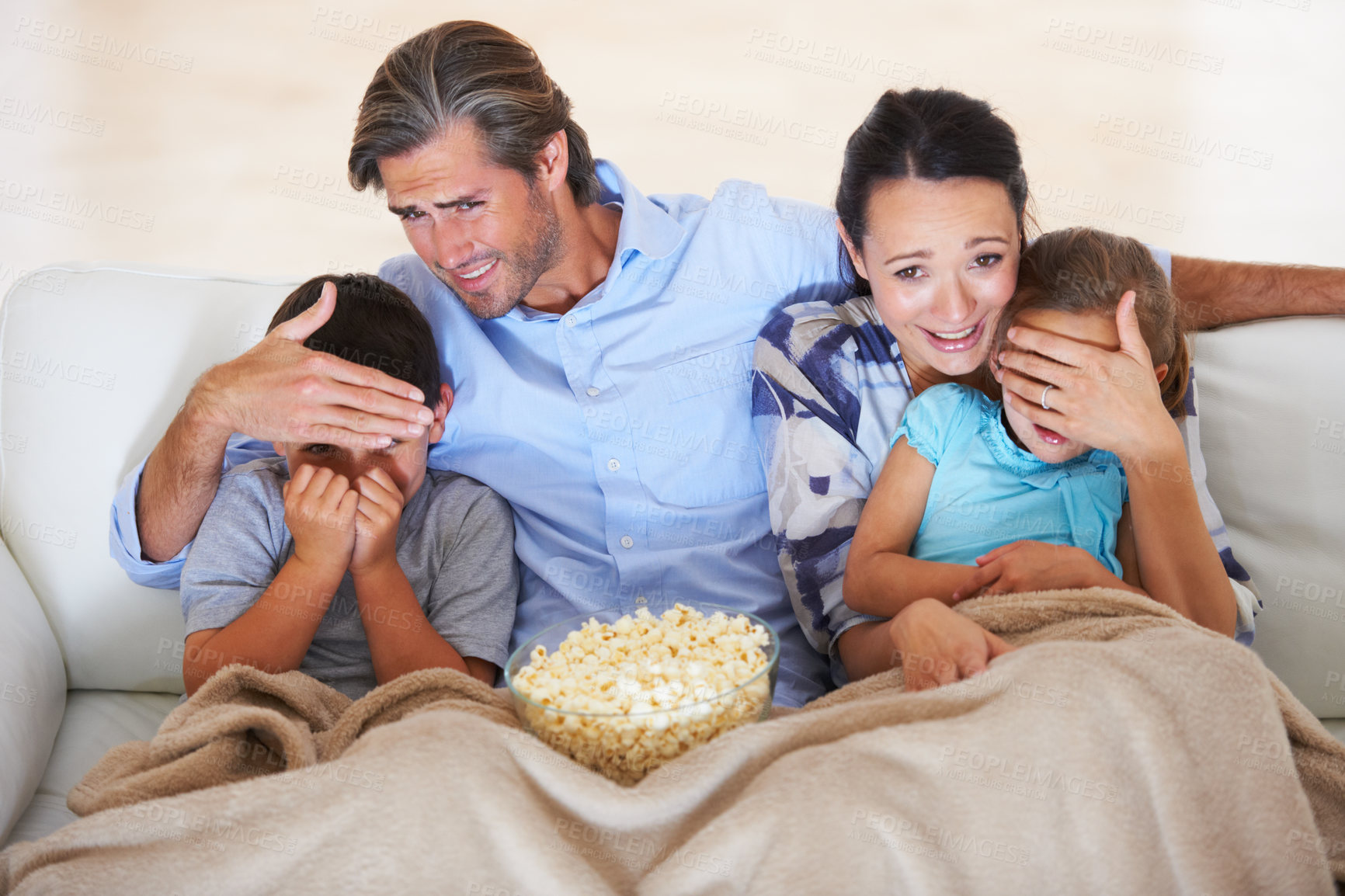 Buy stock photo Two parents covering their children's eyes while watching a scary movie