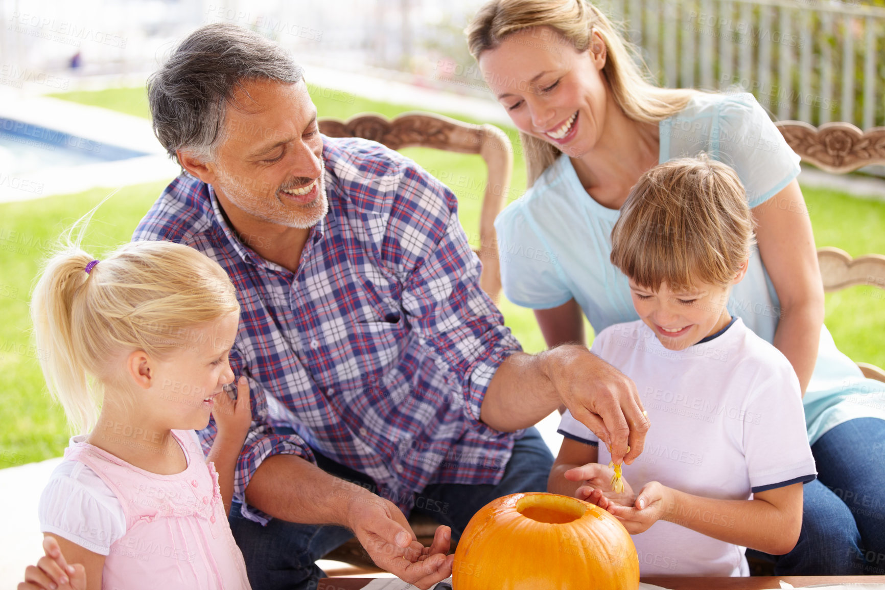 Buy stock photo Halloween, family and carving a pumpkin with children outdoor in home backyard for fun and bonding. Man and woman or parents and young kids together for creativity, holiday lantern and happy craft