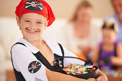 Buy stock photo A little boy dressed in a pirate costume and holding a basket of sweets with family sitting in the background