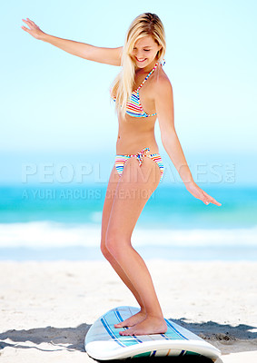 Buy stock photo A pretty blonde in her bikini balancing on her surfboard in the sand