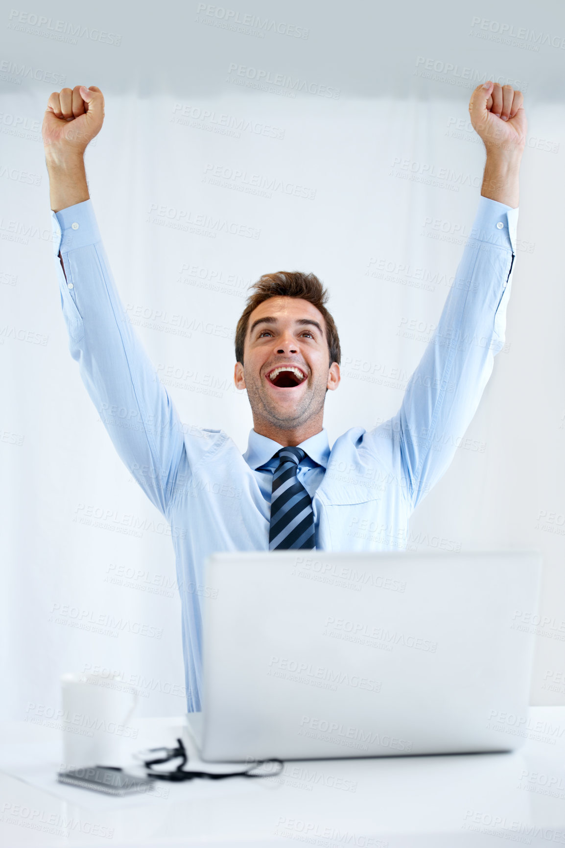Buy stock photo A businessman sitting at his desk with his computer in front of him and cheering with his arms raised above his head