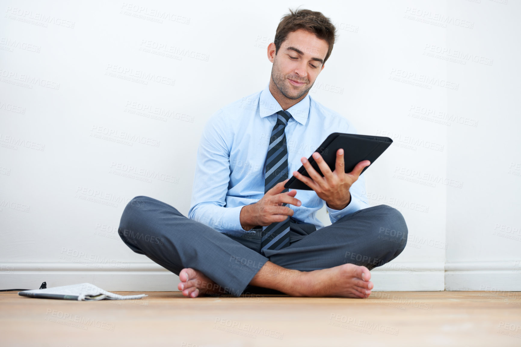 Buy stock photo A barefoot businessman sitting on the floor against a wall and using a digital tablet