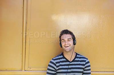 Buy stock photo A handsome young man smiling happily while listening to music through his headphones