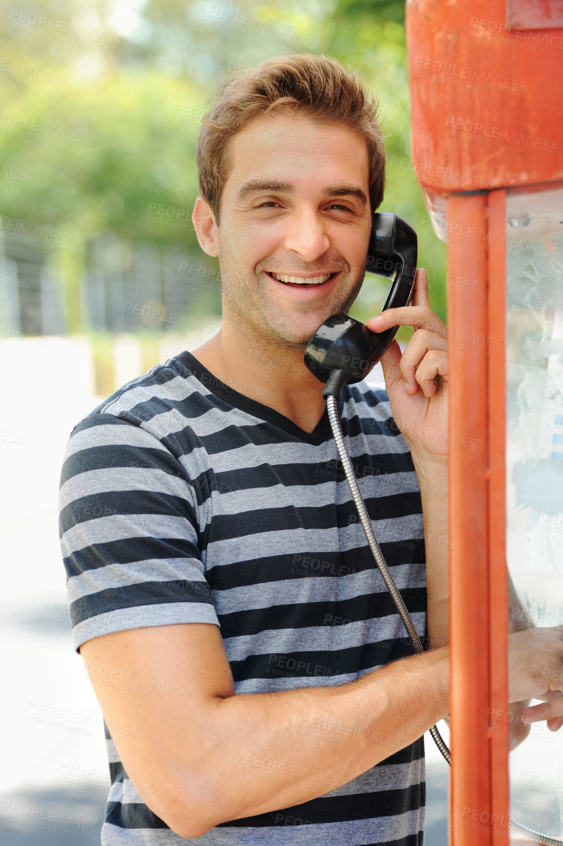 Buy stock photo A handsome young man smiling and having a conversation on a public telephone