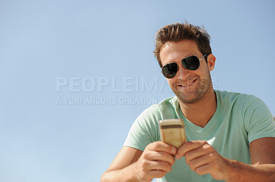 Buy stock photo A smiling young man wearing sunglasses and texting on his cellphone alongside copyspace