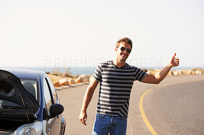 Buy stock photo A handsome young man standing on the side of the road besides his broken-down car and hitching a ride