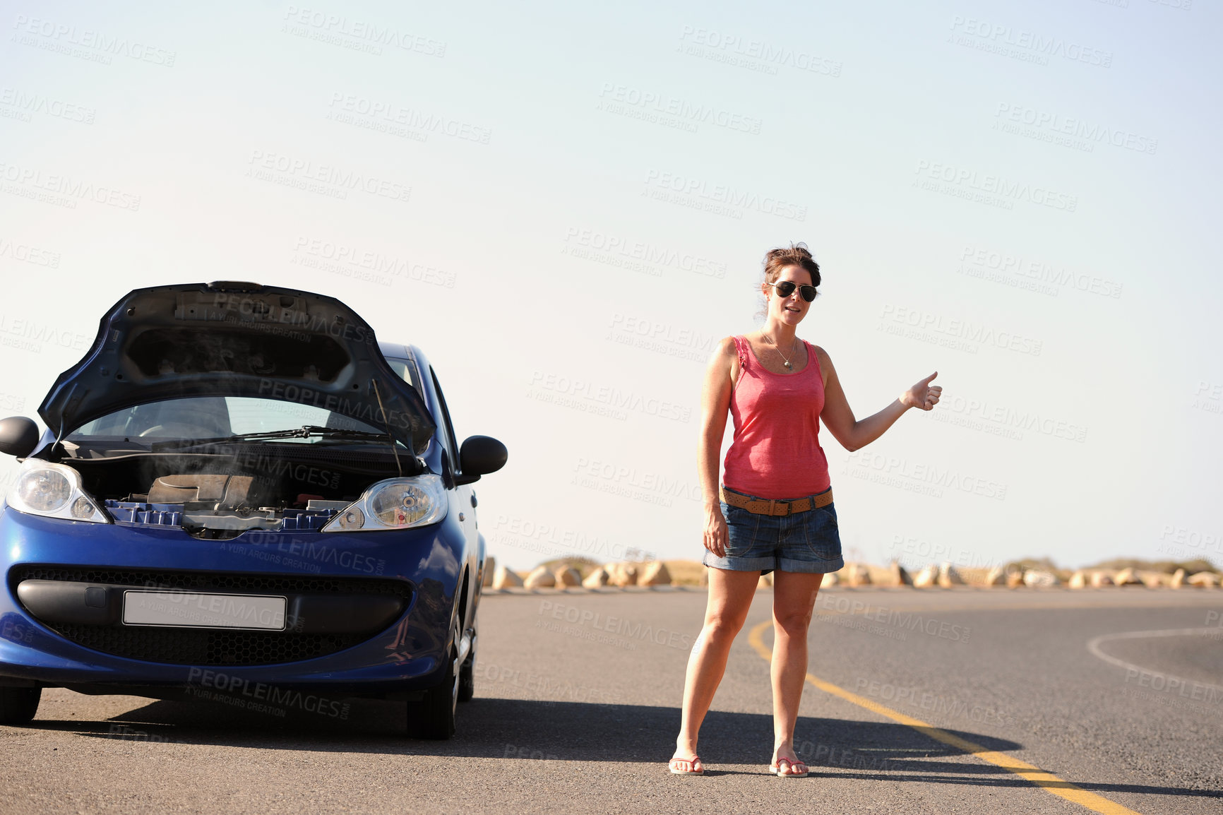 Buy stock photo A beautiful young woman standing with her broken-down car hitching a ride on the side of the road