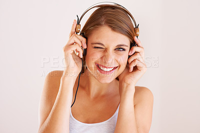 Buy stock photo Woman, portrait and wink with headphones in studio for music, audio subscription or streaming multimedia album on white background. Happy model, blink and listening to podcast, hearing sound or radio