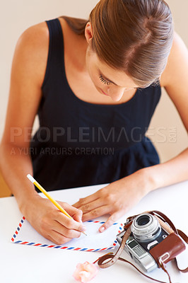 Buy stock photo A young woman writing an address on an envelope with a camera lying on her desk