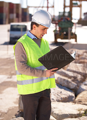 Buy stock photo Shot of a handsome young construction worker reading through the building plans