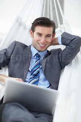 Buy stock photo A young businessman lying on a hammock while working on his laptop