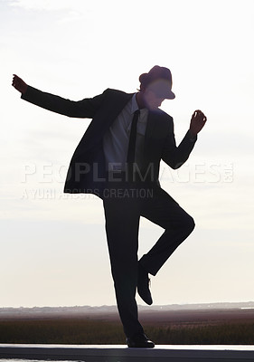 Buy stock photo Silhouette image of a young man in a suit dancing against the morning sky