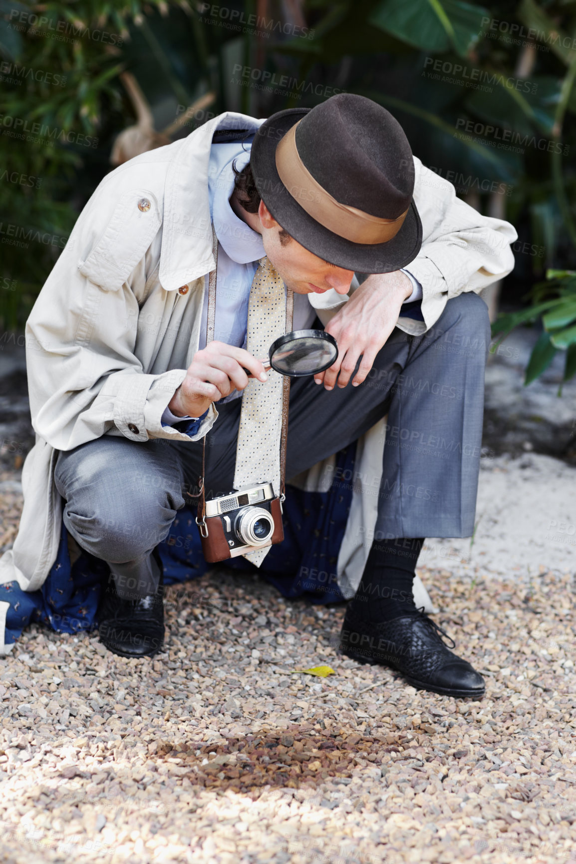 Buy stock photo Curious private investigator looking through a magnifying glass at the ground for clues