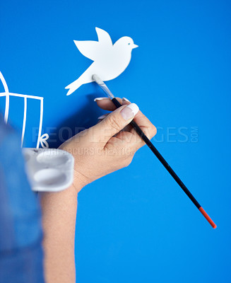 Buy stock photo Closeup of a female artist painting a bird on a blue background