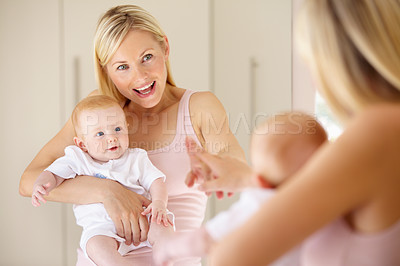 Buy stock photo A cute baby girl looking at herself in the mirror while her mom points
