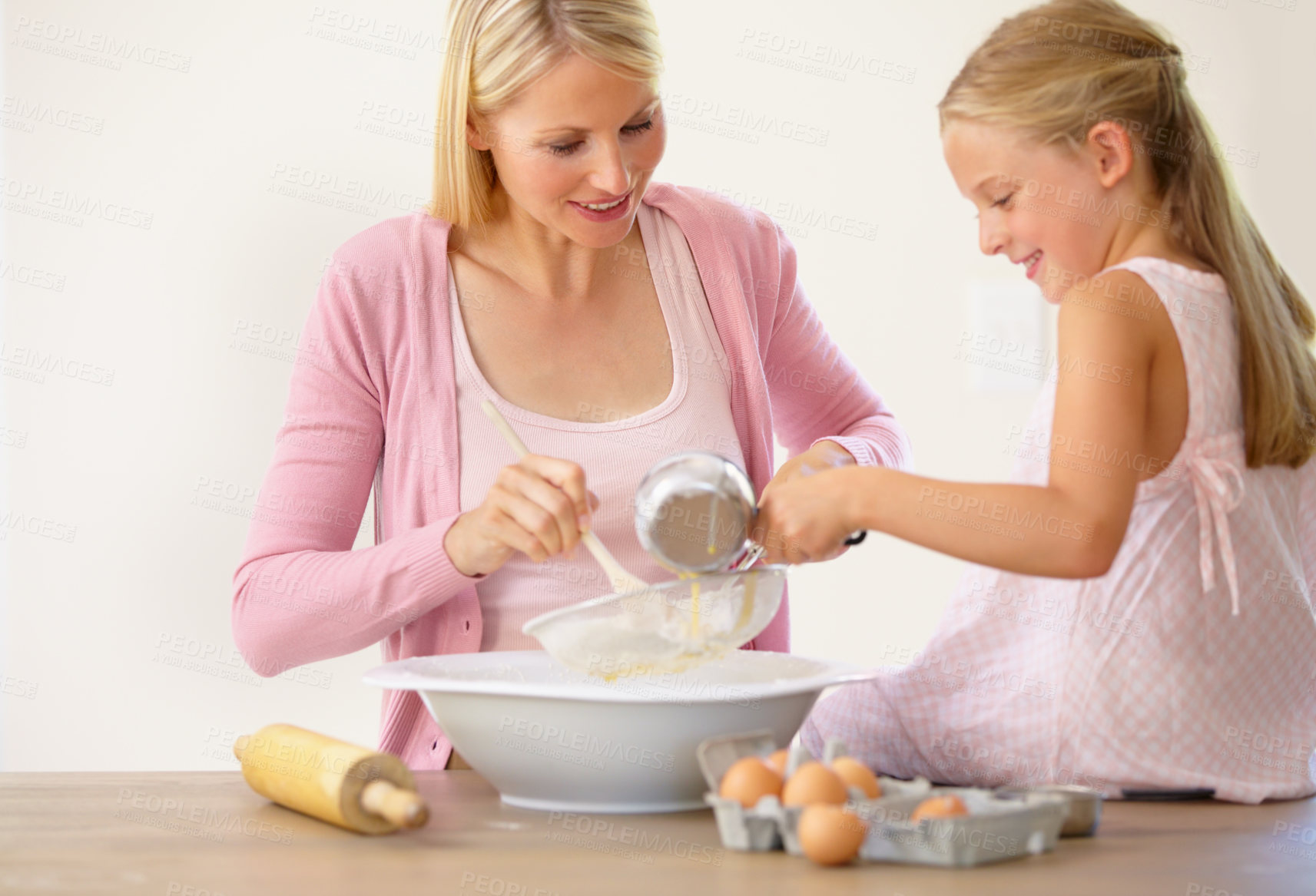 Buy stock photo A little girl sitting on a kitchen counter and helping her mother bake