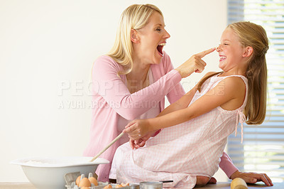 Buy stock photo A mother playfully putting flour on her daughters nose while baking together