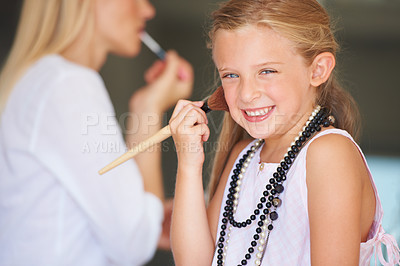 Buy stock photo Little girl trying on her mother's makeup while her mother is in the background