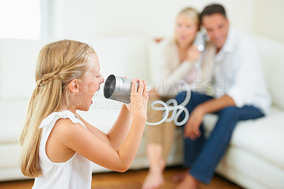 Buy stock photo A little girl shouting loudly into a tin can connected to her parents in the background