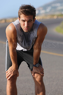 Buy stock photo Tired young runner leaning over to catch his breath