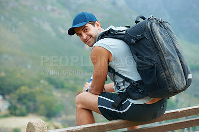 Buy stock photo Handsome young hiker sitting and smiling at the camera with a beautiful view in the background