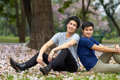 Buy stock photo Cute young gay Asian couple smiling together while sitting in the park