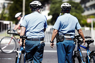 Buy stock photo A cropped rear view shot of two policemen standing with their bicycles