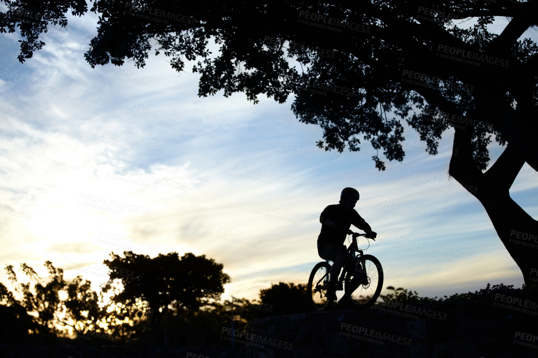 Buy stock photo Silhouette shot of a man riding his bike at dusk