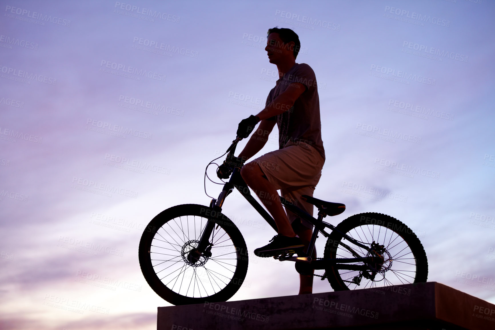 Buy stock photo Silhouette shot of a man riding his bike at dusk