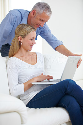 Buy stock photo A beautiful young woman using her laptop with her husband standing behind her