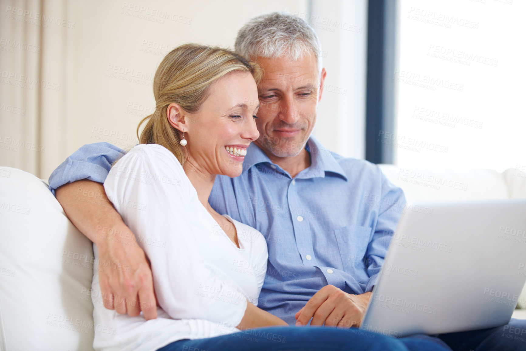 Buy stock photo A young married couple sitting together on the sofa with their laptop