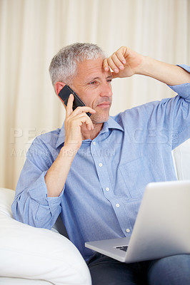 Buy stock photo A mature man sitting on the sofa while using his laptop and cellphone