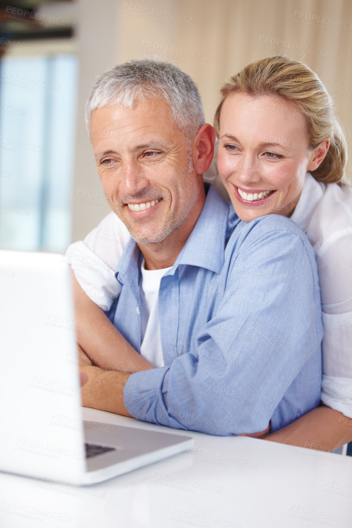 Buy stock photo A wife embracing her husband as he works on the laptop