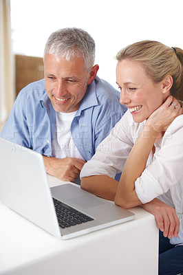 Buy stock photo A mature couple looking happy as they work on their laptop at home