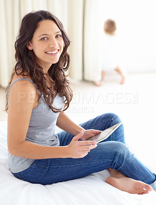 Buy stock photo Portrait of an attractive young mother working on her tablet with her baby in the background