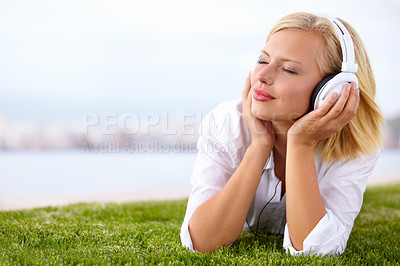 Buy stock photo Shot of a woman lying on a grassy field listening to music with her eyes closed
